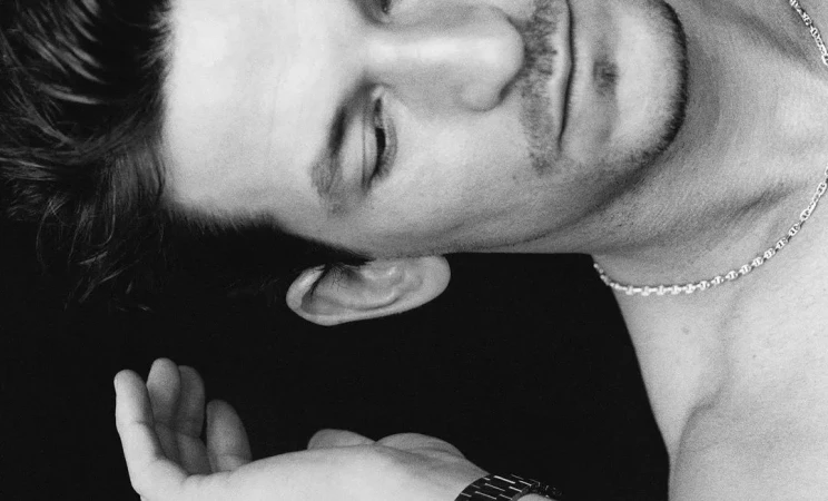 Close-up black and white portrait of a man wearing a silver chain necklace and wrist watch, shot by Paul Scala for Love Want.