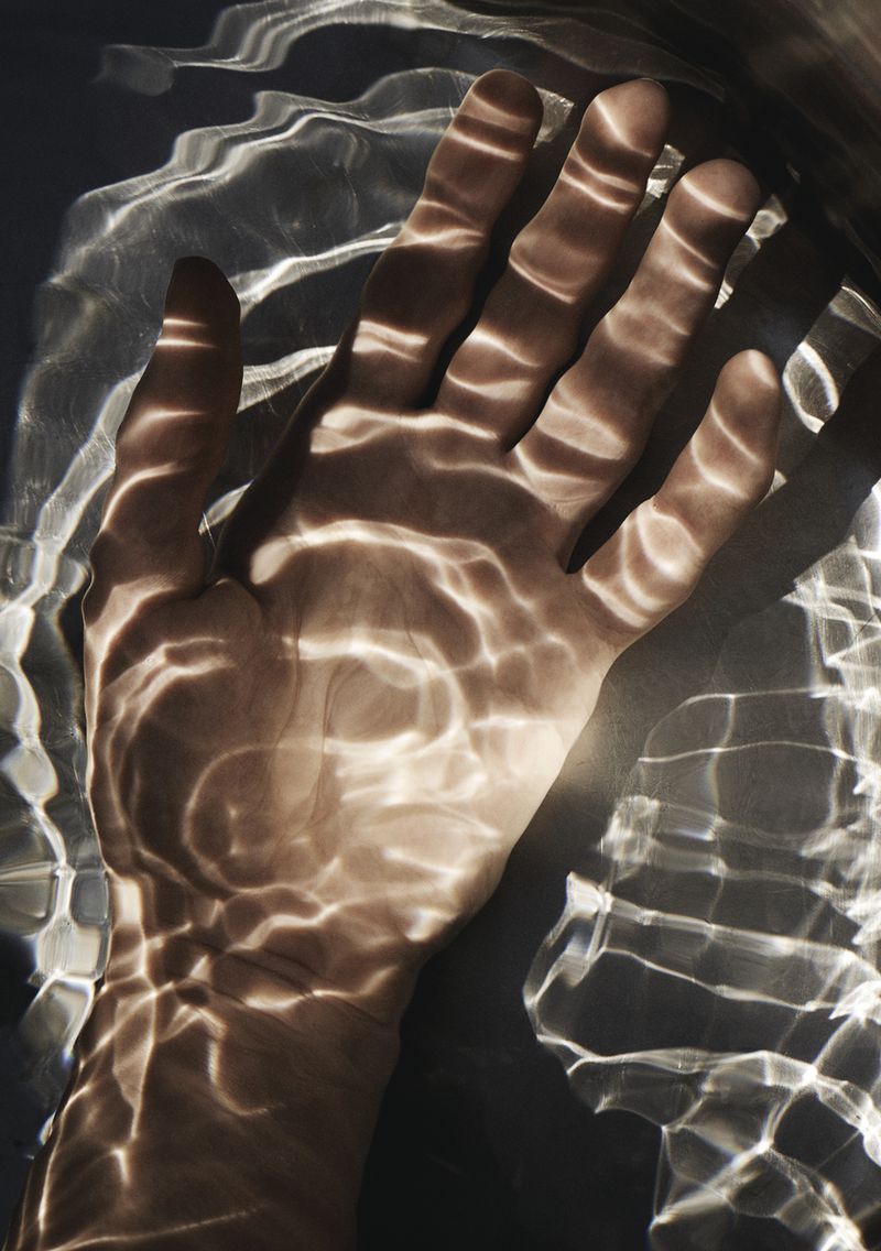 Close-up of a human hand with light patterns projected onto the skin, creating an abstract and textured visual effect.