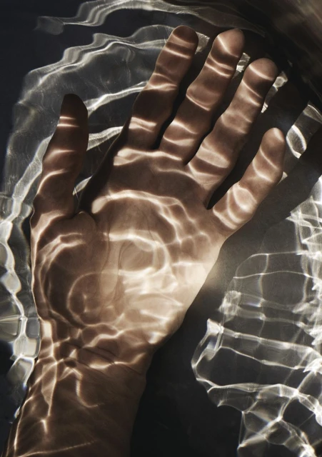 Close-up of a human hand with light patterns projected onto the skin, creating an abstract and textured visual effect.