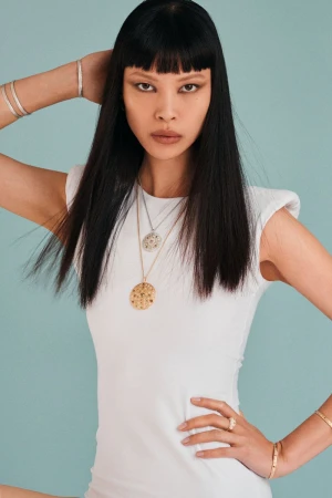 Model Diane Chiu in a white top wearing layered necklaces and bracelets against a teal background for Pop Magazine.