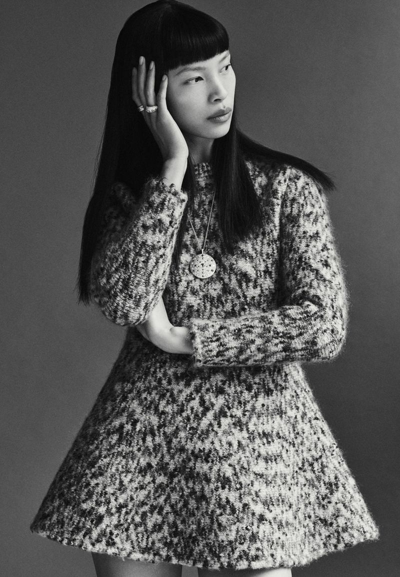 Monochromatic portrait of a stylish Asian woman in a knit dress, accented with a pendant necklace, rings, and a sleek hairstyle.