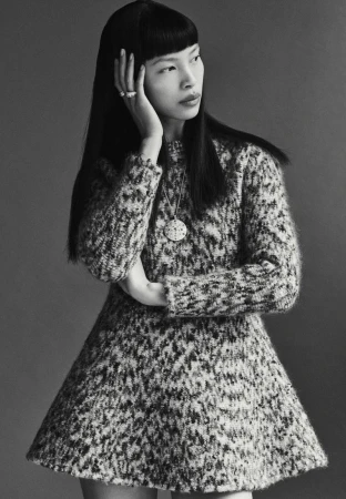 Monochromatic portrait of a stylish Asian woman in a knit dress, accented with a pendant necklace, rings, and a sleek hairstyle.