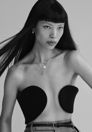 Model Diane Chiu wearing layered necklaces and a black top against a plain light grey backdrop for Pop Magazine.