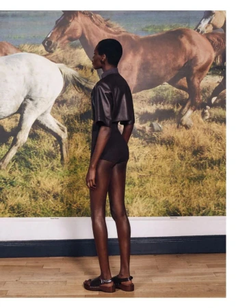 Model Awar Odhiang posing in dark attire against a large painted horse mural for Pop Magazine.