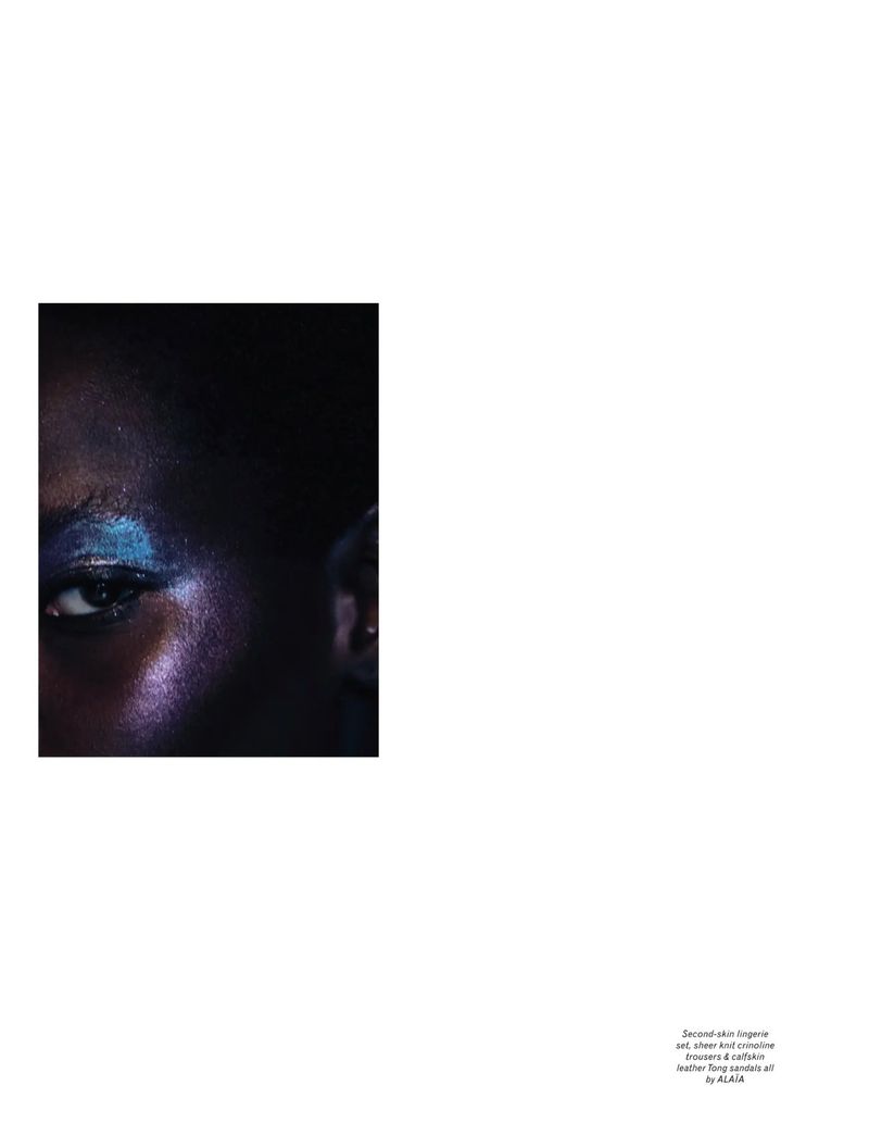 Close-up portrait of a dark-skinned woman with vibrant blue and purple glitter makeup around her eye in a beauty editorial shot.