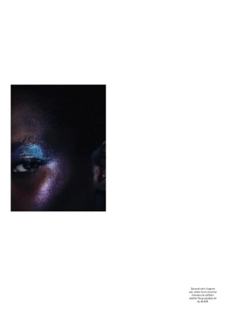 Close-up portrait of a dark-skinned woman with vibrant blue and purple glitter makeup around her eye in a beauty editorial shot.