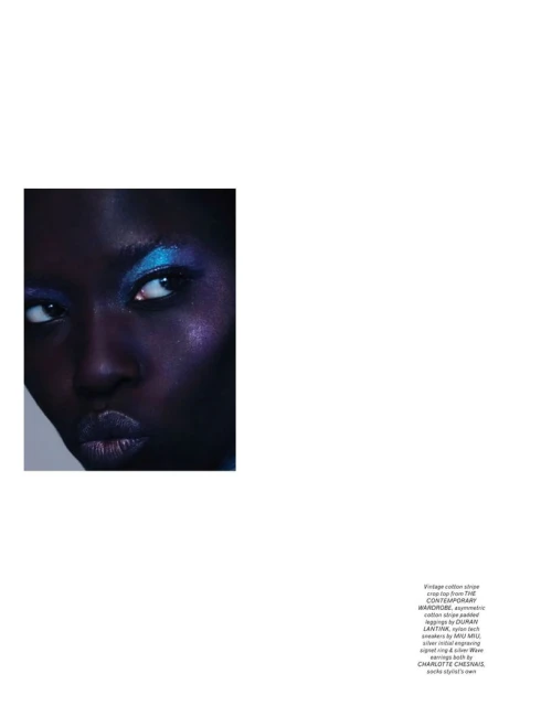 Close-up portrait of a black female model with bright blue eyeshadow and glossy lips. She is posing in a photo studio.