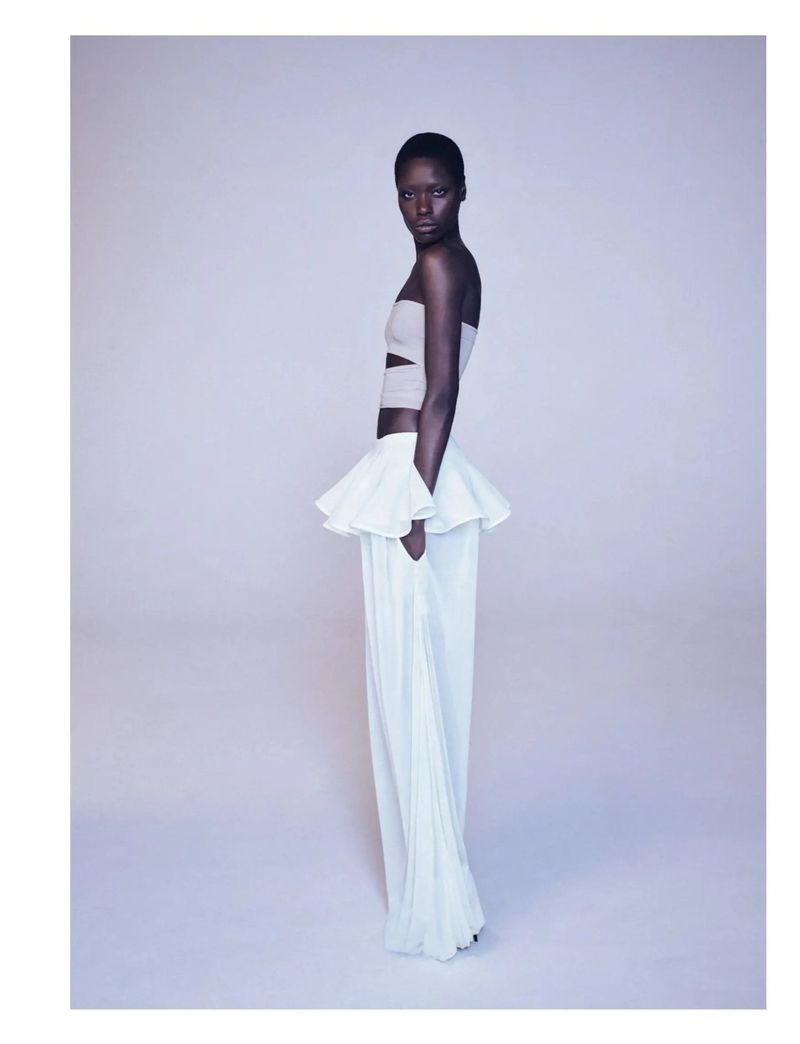 Fashion portrait of an African woman wearing a white strapless top with a ruffle detail and wide-leg white pants, posing in a photo studio.