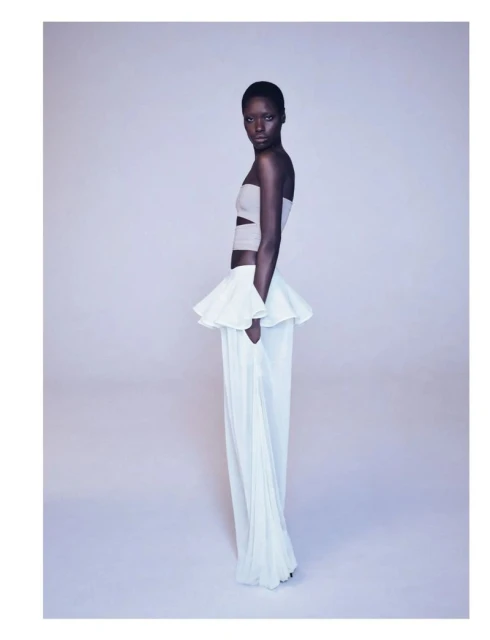Fashion portrait of an African woman wearing a white strapless top with a ruffle detail and wide-leg white pants, posing in a photo studio.