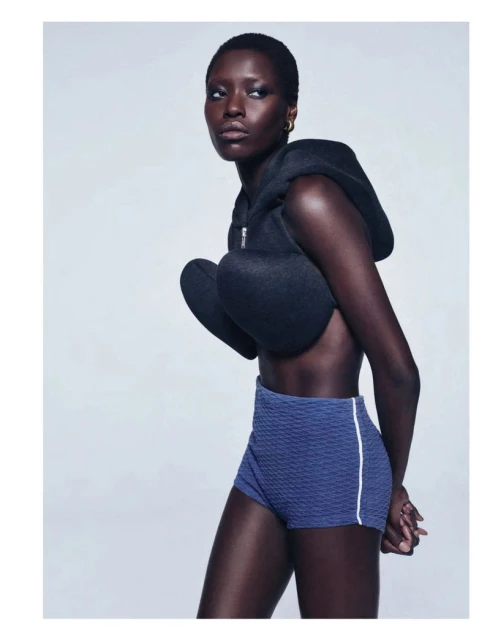 An African woman poses in a studio wearing a black sculpted top and blue shorts with a white stripe in a fashion portrait.