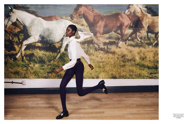 Fashion shot of a Black woman in motion wearing a white top, dark pants, and loafers, in a room with a horse-themed backdrop.