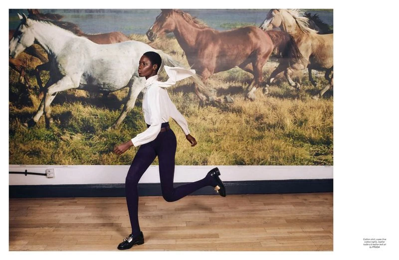 Fashion shot of a Black woman in motion wearing a white top, dark pants, and loafers, in a room with a horse-themed backdrop.
