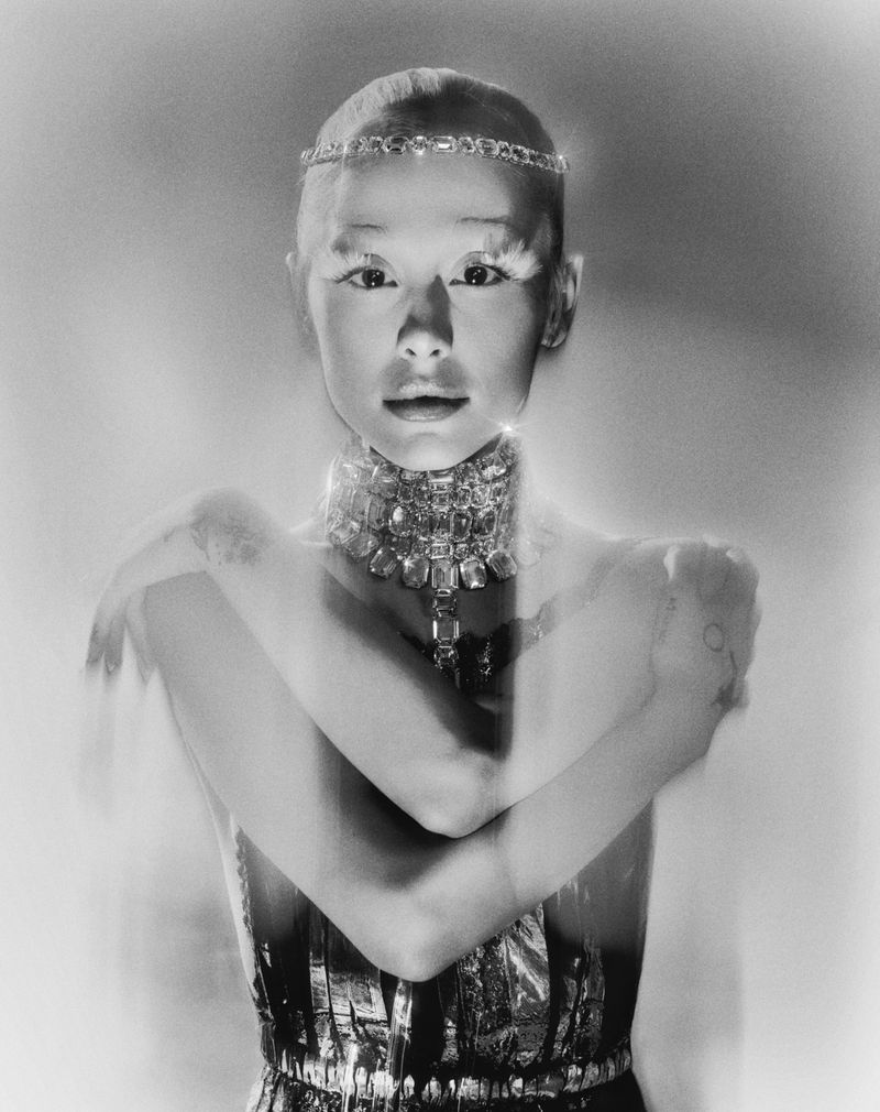 Close-up black and white studio shot of a young adult female model wearing a jeweled headpiece and ornate diamond necklace posing.