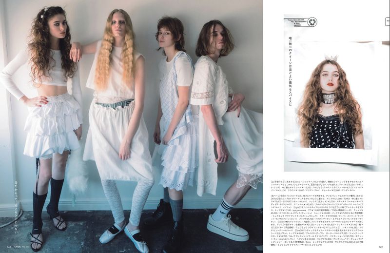 A group of four female fashion models in predominantly white clothing posing indoors, with a magazine cutout of another model.