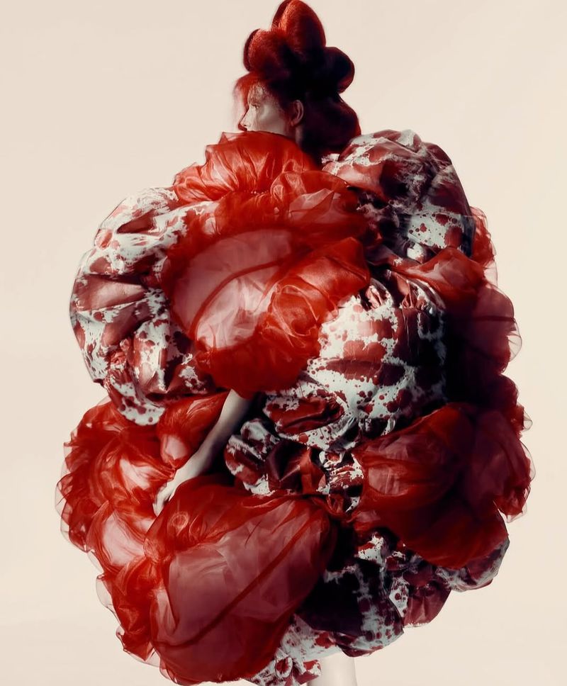 Person in a sculptural fashion dress with white and red patterns against a light background in a studio fashion photoshoot.