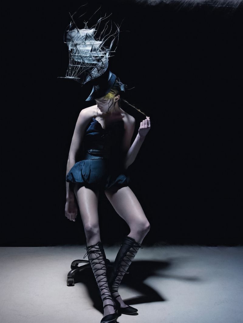 A woman in a dress with a ship sculpture on her head, captured in a dramatic studio portrait with dark background and artful lighting.