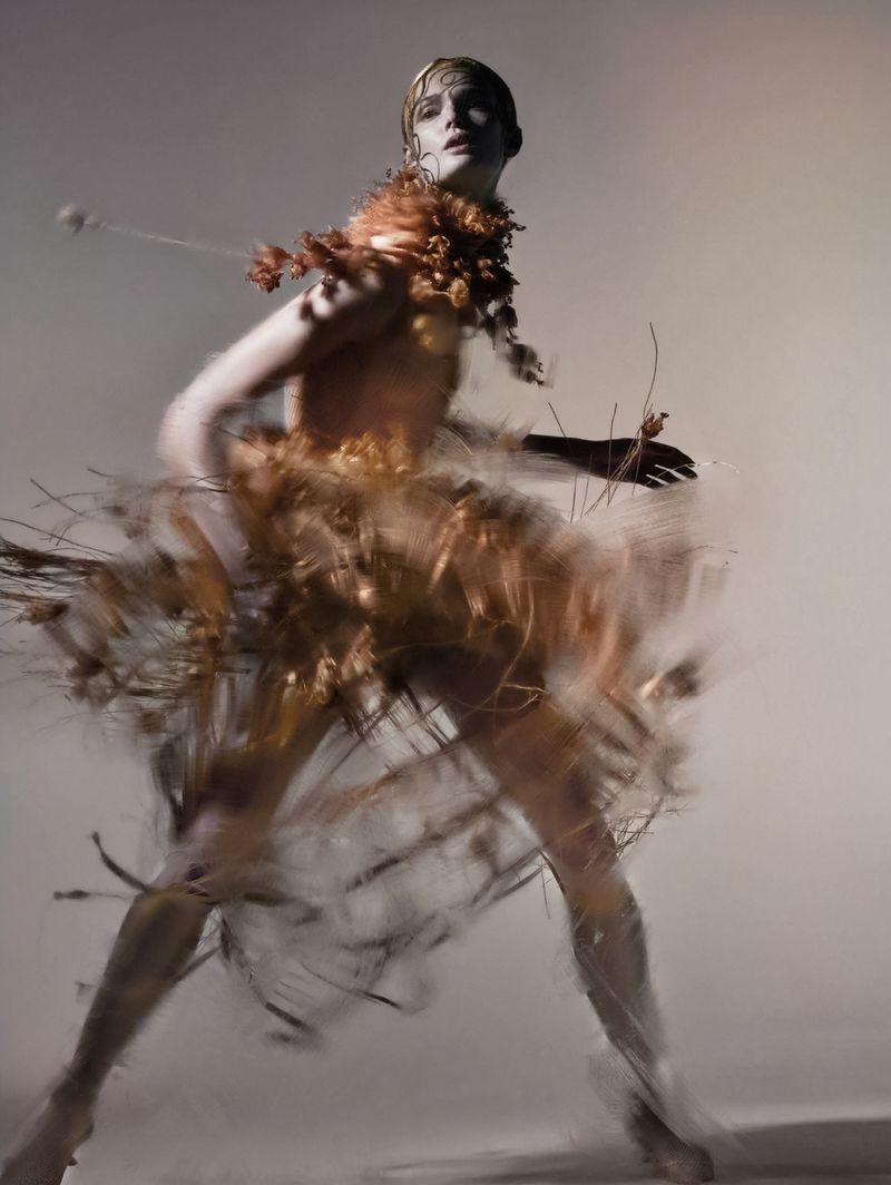 Person in couture dress with organic material, photographed with long exposure against a neutral background in a studio shot.