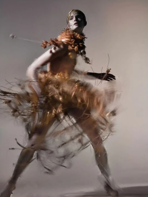 Person in couture dress with organic material, photographed with long exposure against a neutral background in a studio shot.