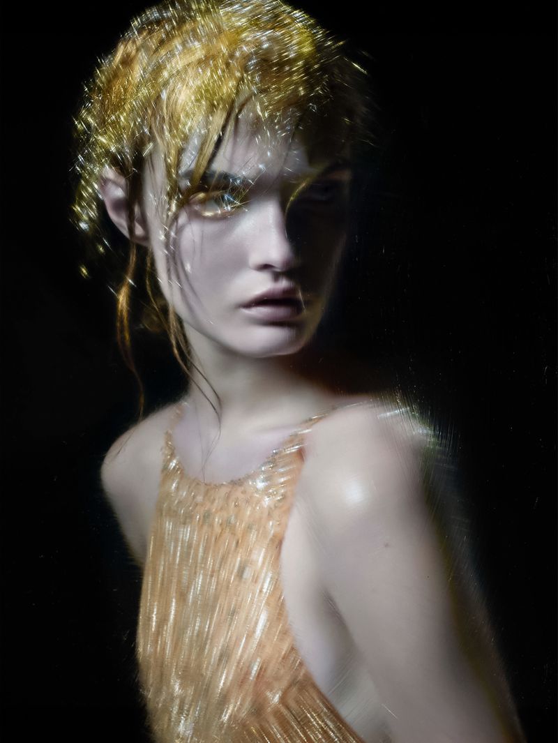 A young woman with gold-glitter hair and a golden dress poses against a black backdrop in a fashion-style portrait, capturing a dramatic effect.