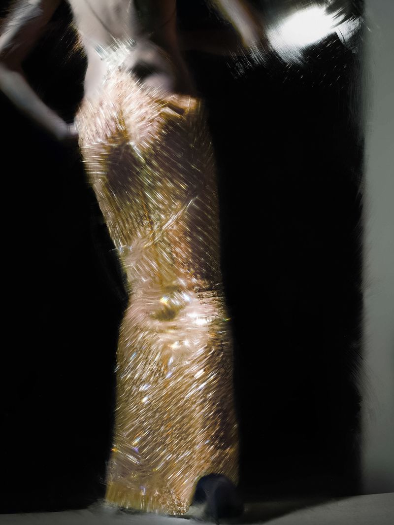 Abstract fashion photograph of a person in a gold beaded dress with a dark background in a blurred, dynamic style, eye-level angle.