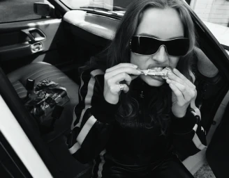Monochrome image of a woman wearing sunglasses eating inside a car