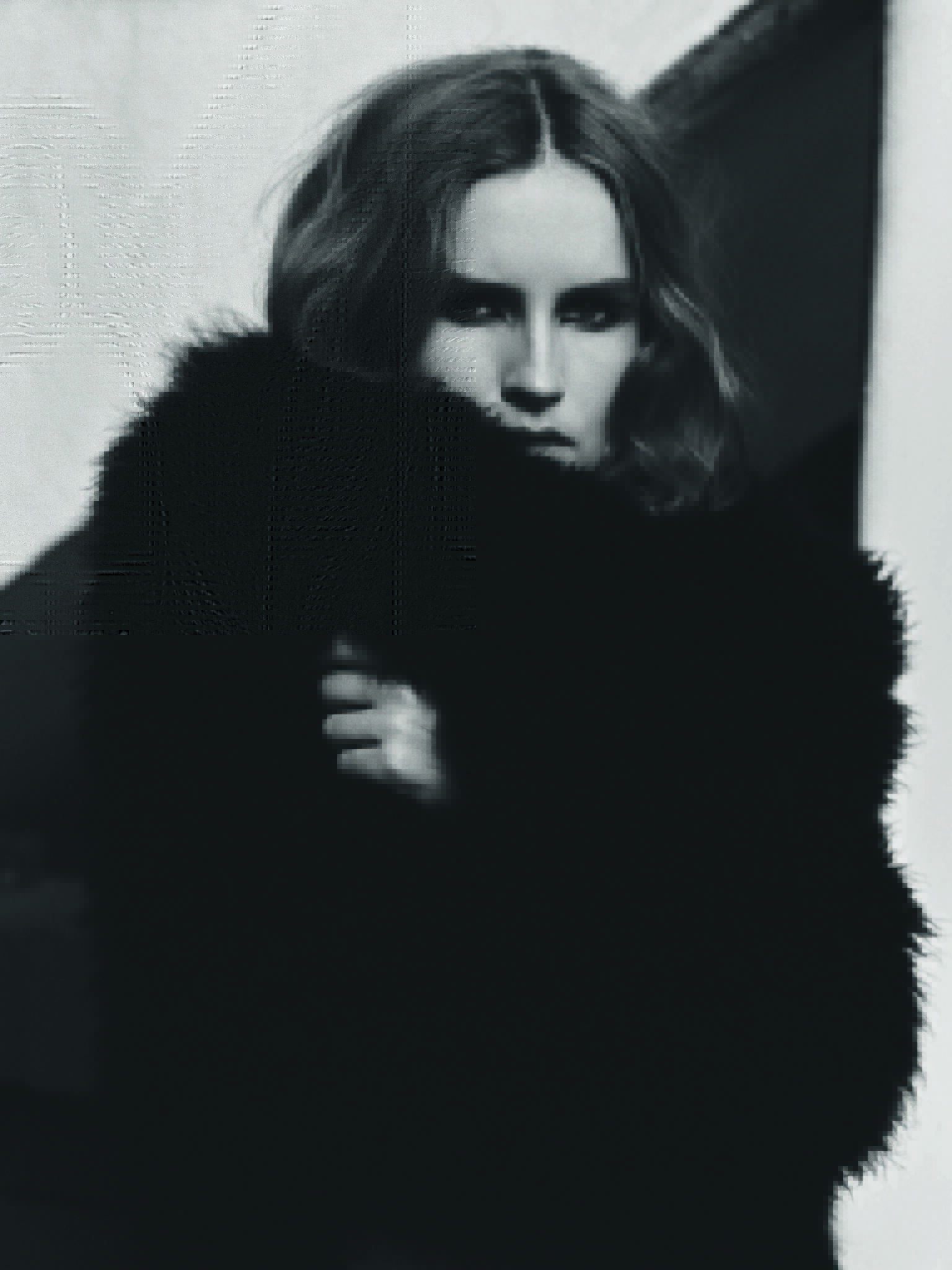 Monochrome portrait of an adult female with shoulder-length wavy hair wearing a dark fur coat against a neutral background.