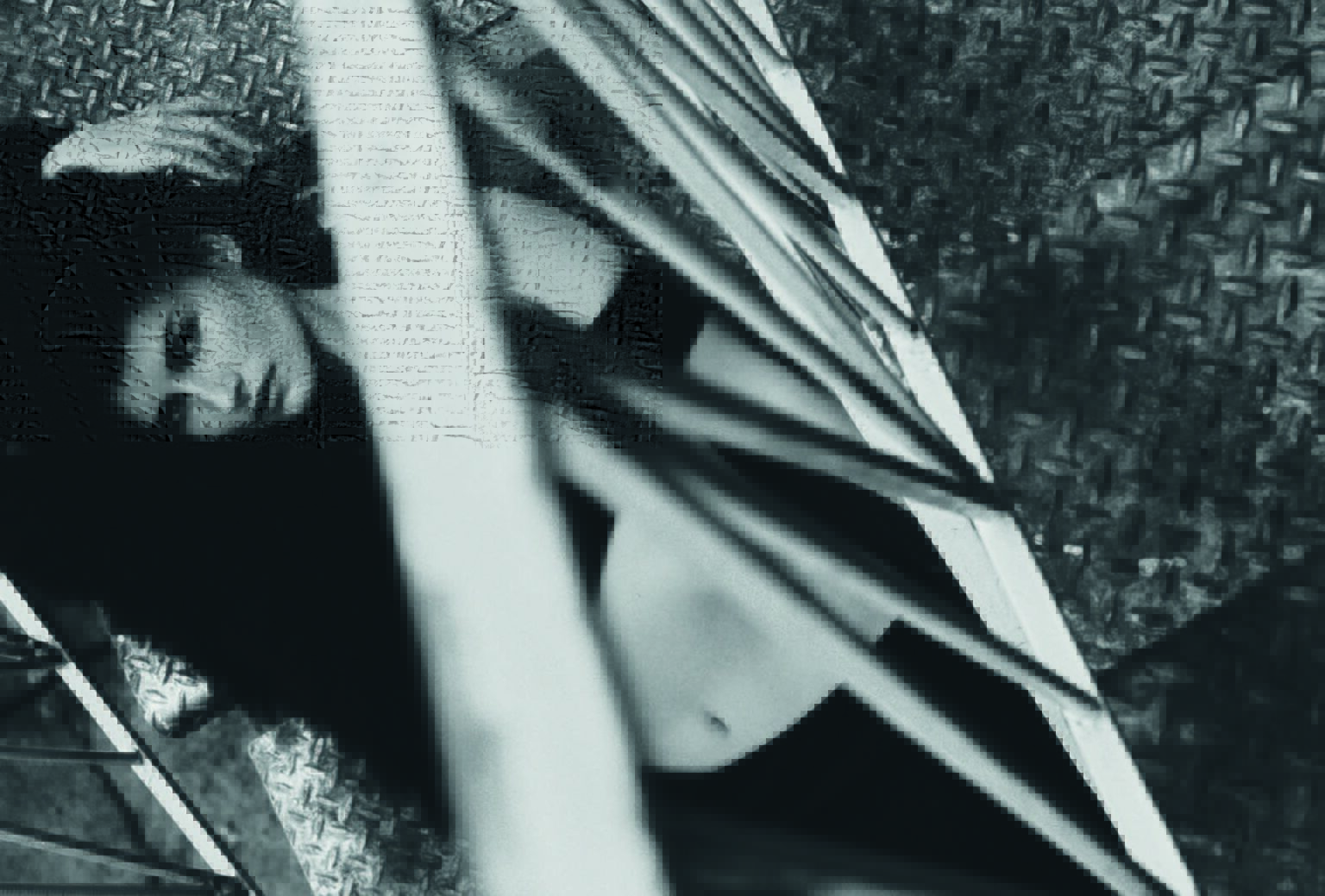 Black and white fashion portrait of a woman lying on a diamond plate surface behind metal bars, showcasing a raw and industrial aesthetic.