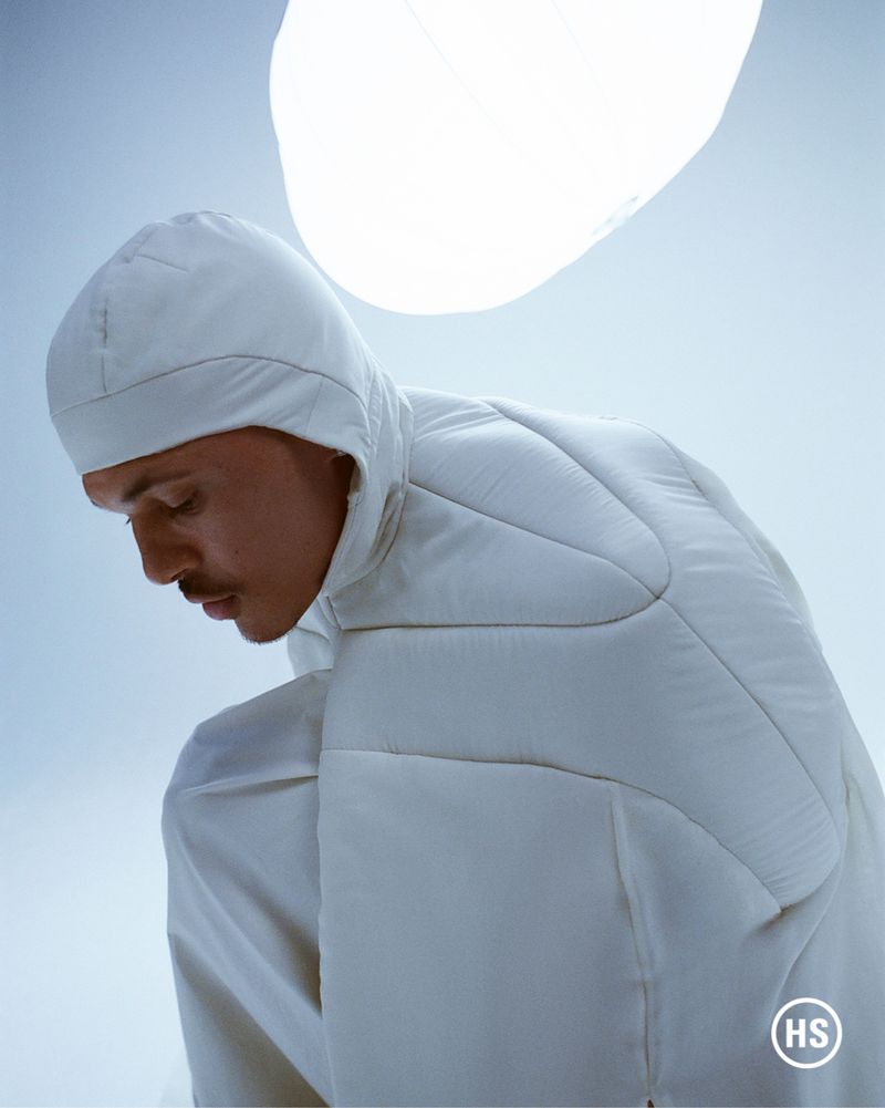 Man with light skin wearing a hooded white puffer jacket in a studio with bright overhead lighting. Fashion, winter clothing concept.