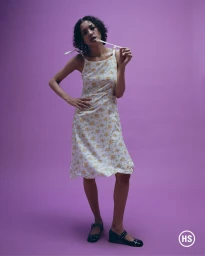 Model in a floral strap dress posing against a solid purple studio backdrop