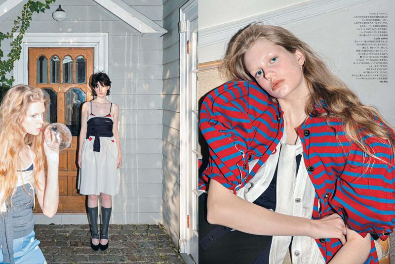 Two young women pose outside a house, one blowing bubbles, the other standing in a black and white dress and black platform shoes.