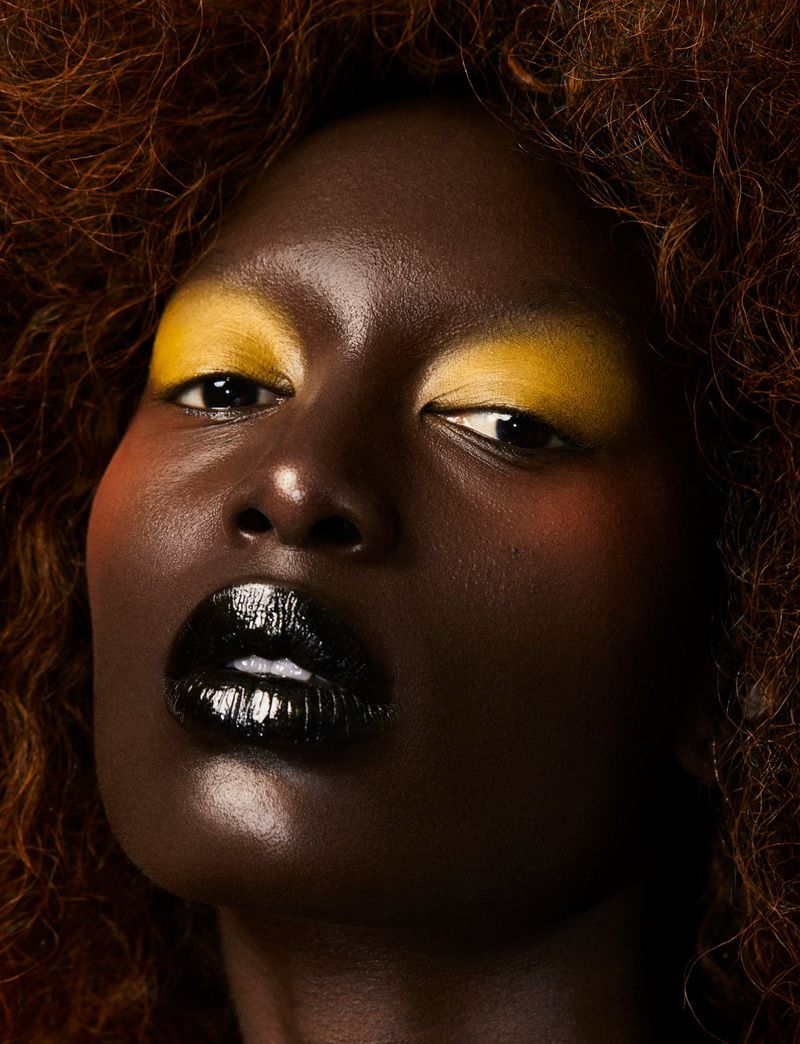 Portrait of a dark-skinned woman with afro and yellow eyeshadow, wearing black lipstick. Close-up shot emphasizing beauty and makeup.