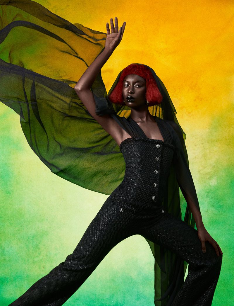 Fashion shot of an African American woman in a sparkly black outfit with red hair posing against a textured yellow-green background.