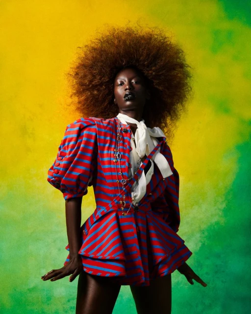 Portrait of an African woman with a large afro wearing a red and blue striped dress with a white bow in front of a yellow and green background.