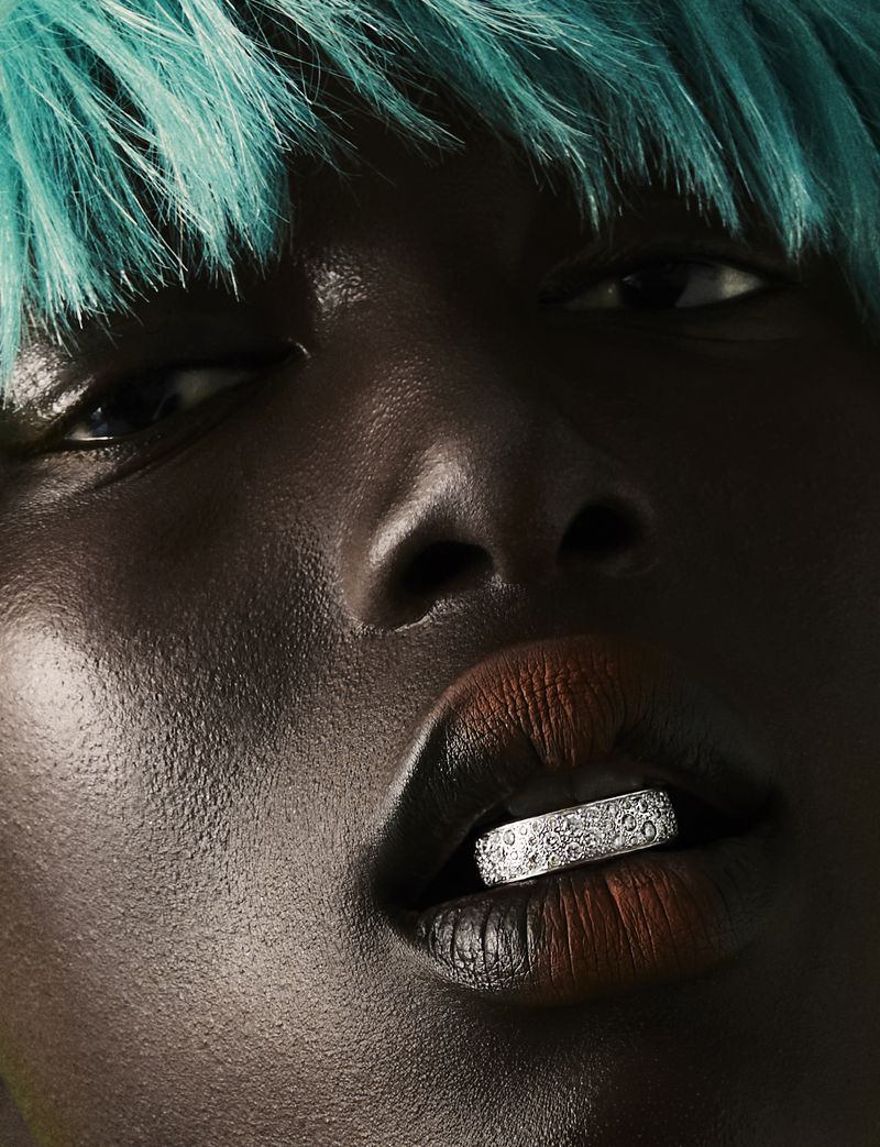 Close-up of a dark-skinned woman with bright turquoise hair and an elaborate silver grill covering her bottom teeth for beauty or fashion concept.