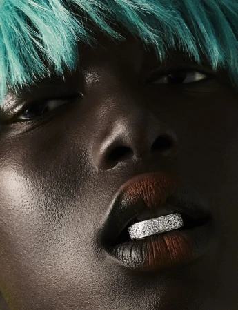 Close-up of a dark-skinned woman with bright turquoise hair and an elaborate silver grill covering her bottom teeth for beauty or fashion concept.