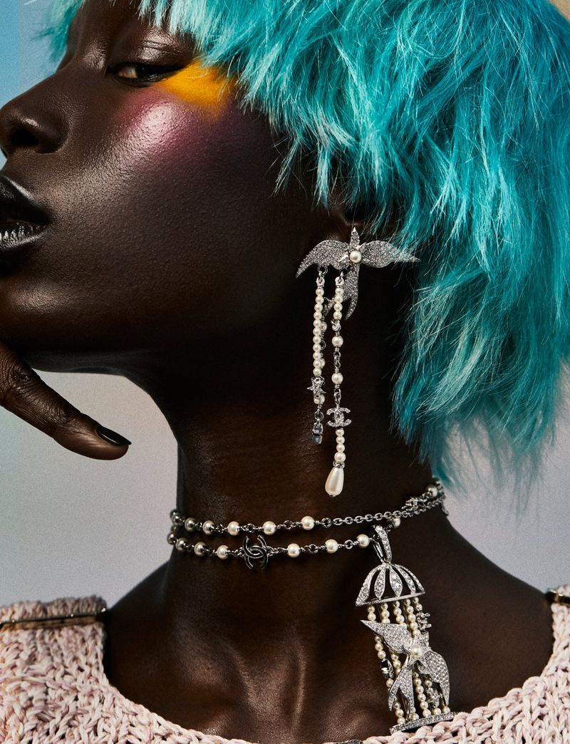 Close-up of a Black female fashion model with bright blue hair wearing pearl jewelry and makeup with yellow and pink eyeshadow.