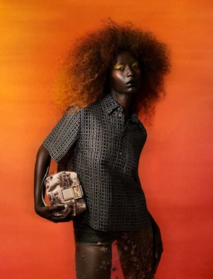 Model with voluminous curly hair holding an embellished handbag against a warm orange gradient background