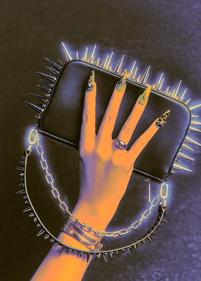 Hand holding a black spiked leather bag with a chain strap against a textured dark background with a blue glow effect
