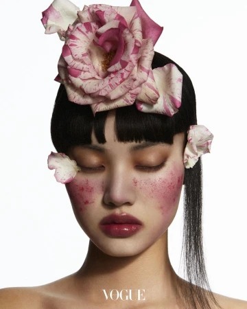 Close-up beauty shot of an Asian woman with closed eyes, wearing floral headpiece and pink blush, set against a bright white background.