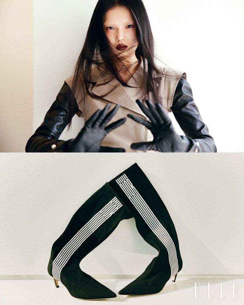 Editorial fashion portrait of a fair-skinned Asian woman with dark lipstick and leather gloves, and striped heeled boots in a photo studio.
