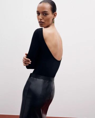 Woman posing in a black long-sleeve top and leather pencil skirt against a neutral backdrop in a fashion studio setting. 
