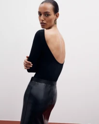 Model in black scoop-back top and dark leather skirt looking back over her shoulder against a white seamless background