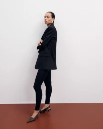 Model wearing a black blazer and slim trousers with dark slingback heels against a studio background.
