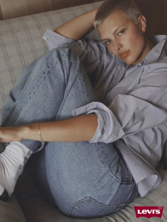 Model with short hair wearing a striped shirt and blue jeans seated on a patterned sofa