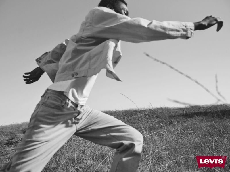 Monochromatic image of a man in a denim jacket and jeans running through a grassy field under a bright sky, featuring Levi's logo.