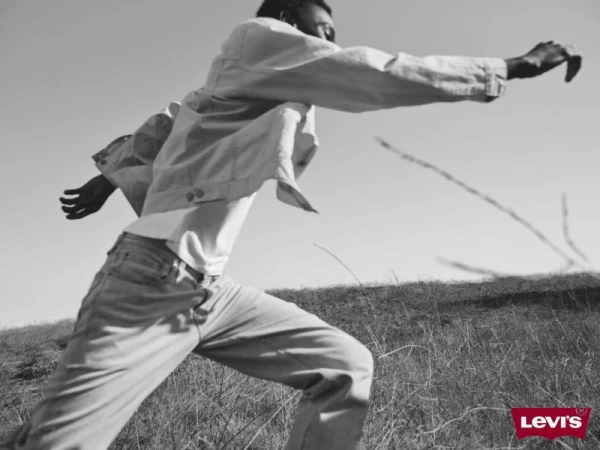 Monochromatic image of a man in a denim jacket and jeans running through a grassy field under a bright sky, featuring Levi's logo.