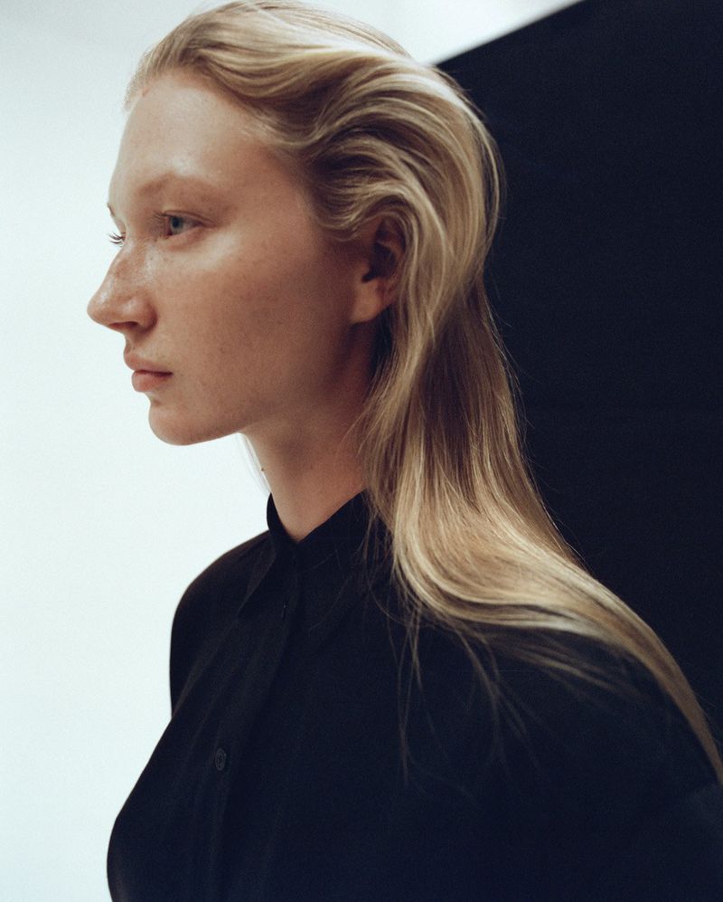 Portrait of a young adult female model in a black button-down shirt, posing in profile against a stark black and white backdrop.