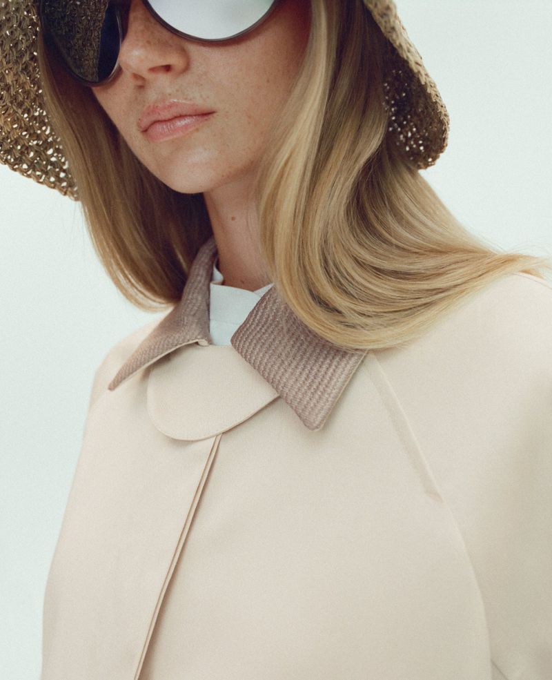 Woman in beige coat, white shirt, straw hat, and sunglasses. Close-up shot. Fashion editorial style. Neutral color palette.