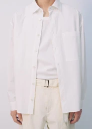 Model wearing an unbuttoned white shirt, layered over a white tank top and cream belted trousers against a plain seamless background.