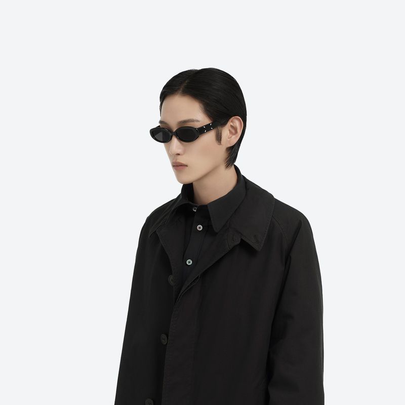 Model wearing black sunglasses and a dark buttoned jacket against a clean white background for Maison Margiela and Gentle Monster